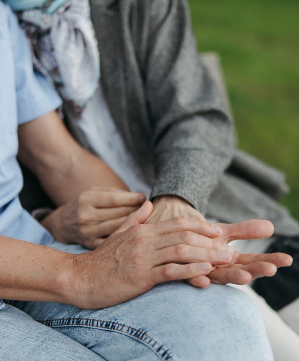 Two pairs of hands resting together on a lap, outdoors.
